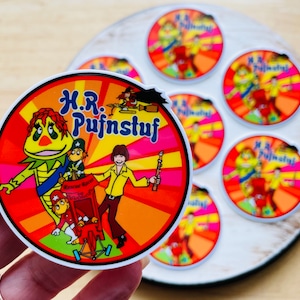 May include: A set of eight round stickers featuring a cartoon character named H.R. Pufnstuf. The stickers are colorful and feature a variety of characters from the show, including H.R. Pufnstuf, the green and yellow creature, and a red and white robot. The stickers are perfect for adding a touch of nostalgia to your belongings.