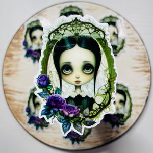 Könnte beinhalten: Ein Aufkleber mit einer gotischen Illustration eines Mädchens mit dunklen Haaren und großen Augen. Sie trägt einen weißen Kragen und ein schwarzes Kleid. Der Hintergrund ist ein grünes und weißes Blumenmuster mit violetten Blumen.