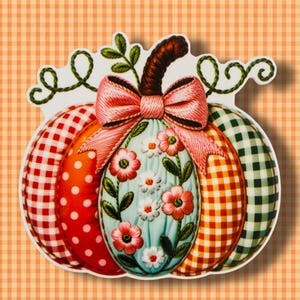 May include: A decorative pumpkin-shaped design with a variety of patterns and textures. The pumpkin features sections of red polka dots, orange, and green and orange gingham. A light blue center is adorned with embroidered flowers and a pink bow.