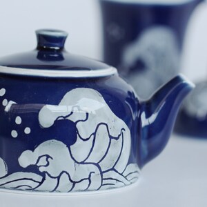 May include: A blue ceramic teapot with a white wave design. The teapot has a lid and a spout.