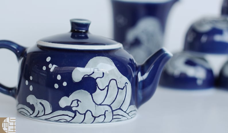 May include: A blue ceramic teapot with a white wave design. The teapot has a lid and a spout.