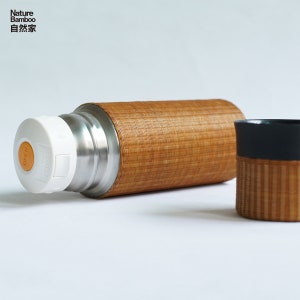 Puede incluir: Un termo de acero inoxidable con un exterior de bamb&uacute;. El termo tiene una tapa blanca con un bot&oacute;n amarillo. El termo est&aacute; al lado de una taza de bamb&uacute; con un borde gris oscuro.