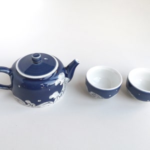 May include: A blue and white ceramic teapot with a matching set of two teacups. The teapot has a wave design and the cups have a similar design.