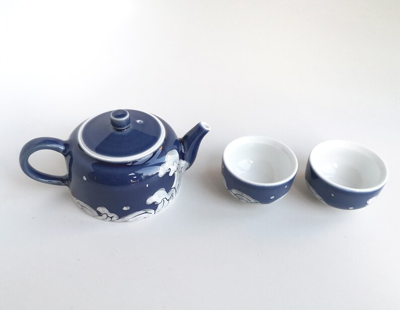 May include: A blue and white ceramic teapot with a matching set of two teacups. The teapot has a wave design and the cups have a similar design.