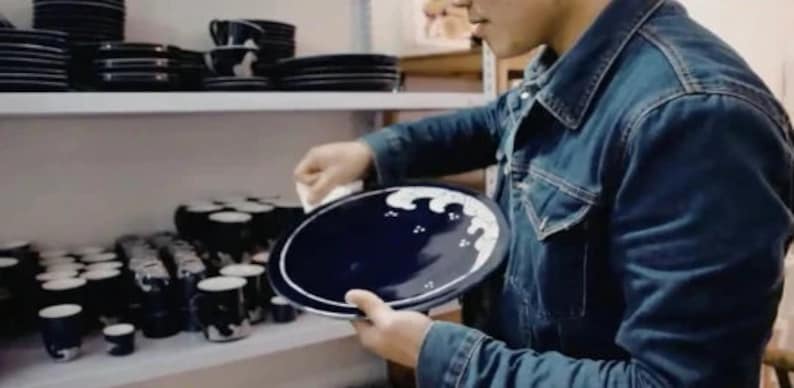May include: A person holding a blue and white ceramic plate with a wave design. The plate is on a shelf with other blue and white ceramic dishes.