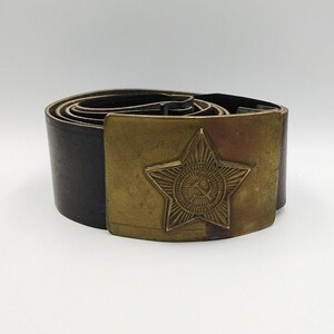 May include: A black leather belt with a brass buckle featuring a five-pointed star with a hammer and sickle inside.
