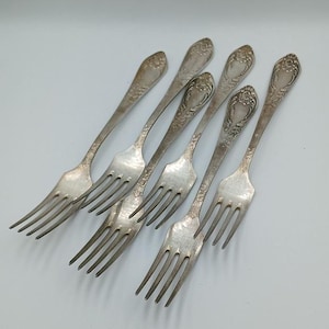 May include: Set of six silver forks with ornate handles. The forks are arranged in a row, with the handles pointing towards the top of the image.