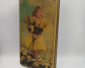 May include: Vintage tin box with a picture of a young girl in a yellow dress holding a bouquet of flowers. The box has a gold trim and a faded, worn look.
