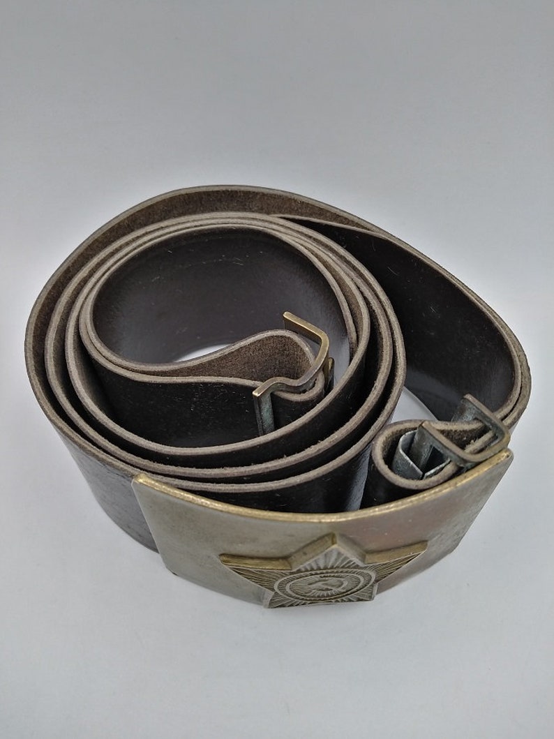 May include: A brown leather belt with a metal buckle featuring a five-pointed star and a hammer and sickle emblem.