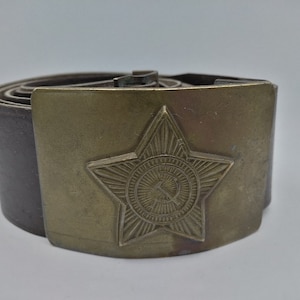 May include: A brown leather belt with a brass buckle featuring a five-pointed star with a hammer and sickle inside.