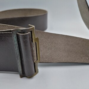 May include: A brown leather belt with a brass buckle. The buckle has a simple design with a rectangular shape and a small, raised lip.