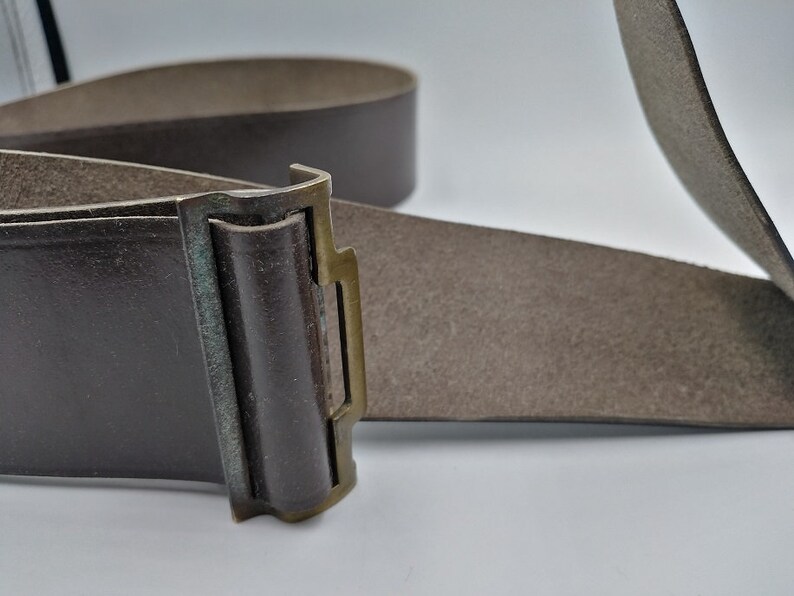 May include: A brown leather belt with a brass buckle. The buckle has a simple design with a rectangular shape and a small, raised lip.