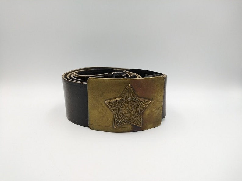May include: A black leather belt with a brass buckle featuring a five-pointed star with a hammer and sickle inside.