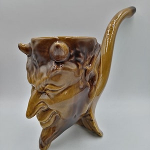 May include: A brown ceramic pipe shaped like a devil's head with a long, curved stem.