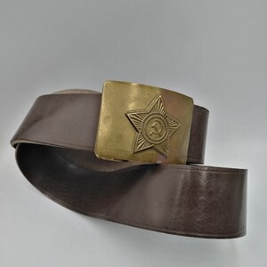 May include: A brown leather belt with a brass buckle featuring a five-pointed star with a hammer and sickle inside.