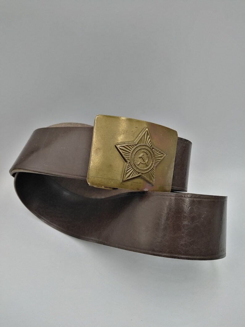 May include: A brown leather belt with a brass buckle featuring a five-pointed star with a hammer and sickle inside.