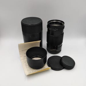 May include: A black camera lens with a lens hood, two lens caps, and a paper instruction manual. The lens has the text "Юпитер-37A" printed on it.