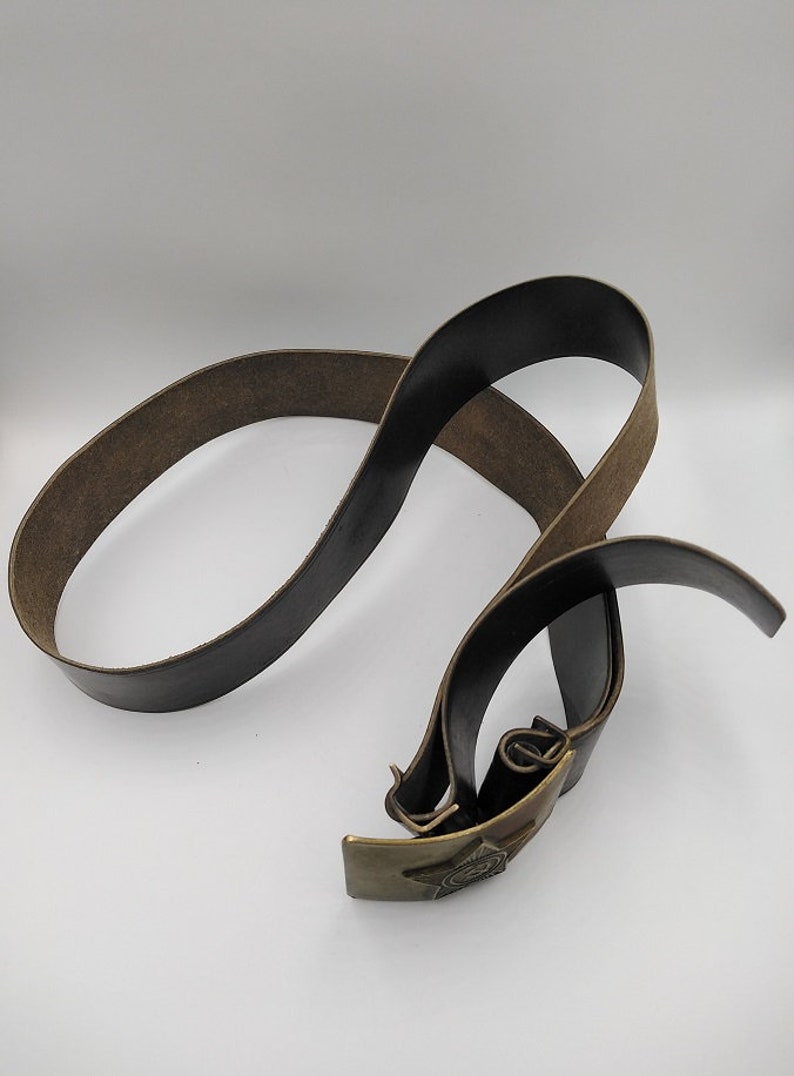 May include: A brown leather belt with a brass buckle featuring a five-pointed star. The buckle has a raised design of a hammer and sickle.