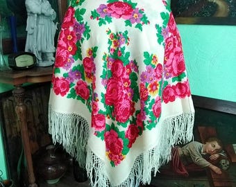 May include: A cream-colored shawl with a vibrant floral pattern in shades of pink, red, purple, and green. The shawl features a fringe trim along the edges. The floral design is centered on the shawl.