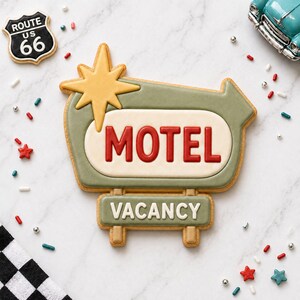 May include: A decorated cookie in the shape of a vintage motel sign with the word "MOTEL" in red letters. The sign is green and cream-colored, with a yellow starburst. A "VACANCY" sign is below. A Route 66 sign cookie is also present.
