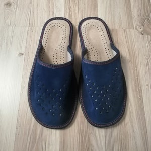 Puede incluir: Un par de zapatillas de ante azul marino. Las zapatillas tienen un dise&ntilde;o perforado en la parte superior, un interior beige claro con peque&ntilde;os orificios de ventilaci&oacute;n y un ribete rojo oscuro. Para uso en interiores.