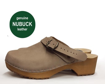 May include: Tan nubuck leather clog with a wooden sole and a buckle strap. The clog has a rounded toe and a small heel. The text "genuine NUBUCK leather" is in a green circle.