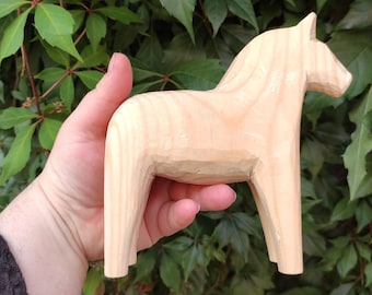 Puede incluir: Una figurita de caballo tallada en madera, también conocida como caballo Dala, es un arte popular sueco tradicional. El caballo es de color marrón claro y tiene un diseño simple y estilizado.