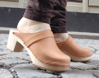 May include: A pair of tan leather clogs with wooden soles and a thick heel. The clogs have a strap across the top of the foot.