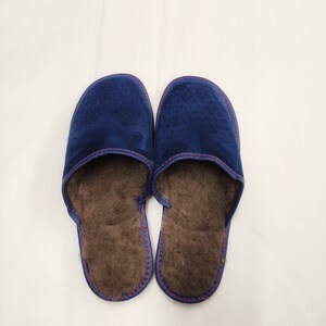 Puede incluir: Un par de zapatillas de ante azul marino con un dise&ntilde;o perforado en la parte superior. Las zapatillas tienen un interior marr&oacute;n y difuso y est&aacute;n cosidas con hilo rosa. Estas c&oacute;modas zapatillas est&aacute;n dise&ntilde;adas para uso en interiores.