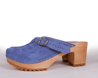 May include: Blue suede clogs with a wooden heel and a buckle strap. The clogs have a white stitch detail around the edge of the sole.