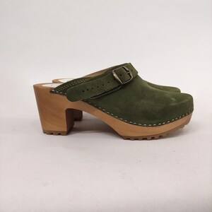 May include: Green suede clog with a buckle strap and a wooden platform heel.