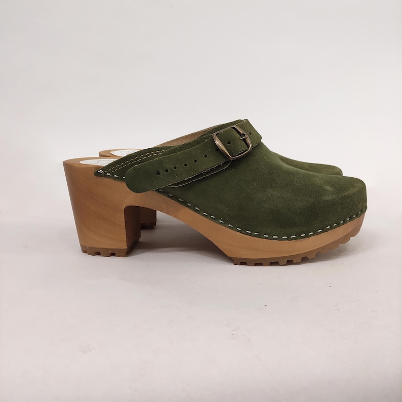 May include: Green suede clog with a buckle strap and a wooden platform heel.