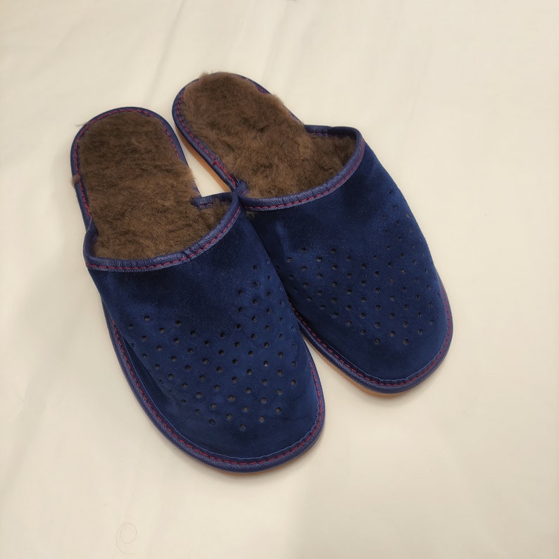 Puede incluir: Un par de zapatillas de ante azul con un dise&ntilde;o perforado. Las zapatillas tienen un interior marr&oacute;n y difuso y un ribete cosido en rojo. Las suelas son de color marr&oacute;n claro. Estas acogedoras zapatillas est&aacute;n dise&ntilde;adas para uso en interiores.