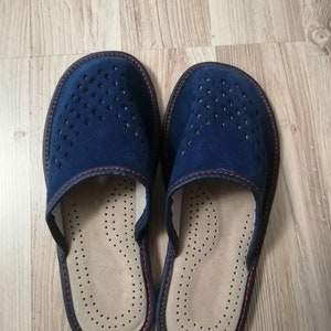Puede incluir: Un par de zapatillas de ante azul marino con un dise&ntilde;o perforado en la parte superior. Las zapatillas tienen una plantilla beige con peque&ntilde;os orificios de ventilaci&oacute;n y un ribete marr&oacute;n oscuro con costuras rojas.