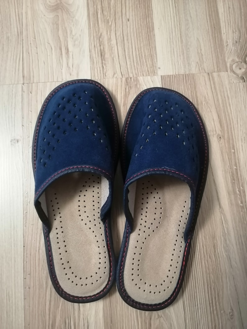 Puede incluir: Un par de zapatillas de ante azul marino con un dise&ntilde;o perforado en la parte superior. Las zapatillas tienen una plantilla beige con peque&ntilde;os orificios de ventilaci&oacute;n y un ribete marr&oacute;n oscuro con costuras rojas.