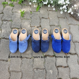 Könnte beinhalten: Drei Paar Wildledersandalen in verschiedenen Blautönen: Jeansblau, Marineblau und Königsblau. Die Sandalen haben Holzsohlen und einen Schnallenriemen.