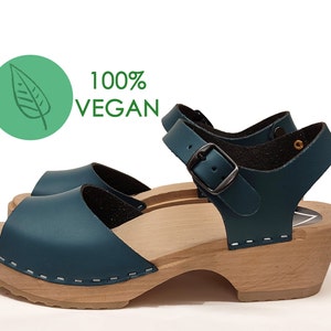 May include: Teal blue leather sandals with a wooden platform sole and an adjustable ankle strap. The sandals are 100% vegan.