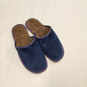 Puede incluir: Un par de zapatillas de ante azul marino con un dise&ntilde;o perforado en la parte superior. Las zapatillas tienen un interior marr&oacute;n y difuso y est&aacute;n ribeteadas con costuras rosas. Estas c&oacute;modas zapatillas est&aacute;n dise&ntilde;adas para uso en interiores.