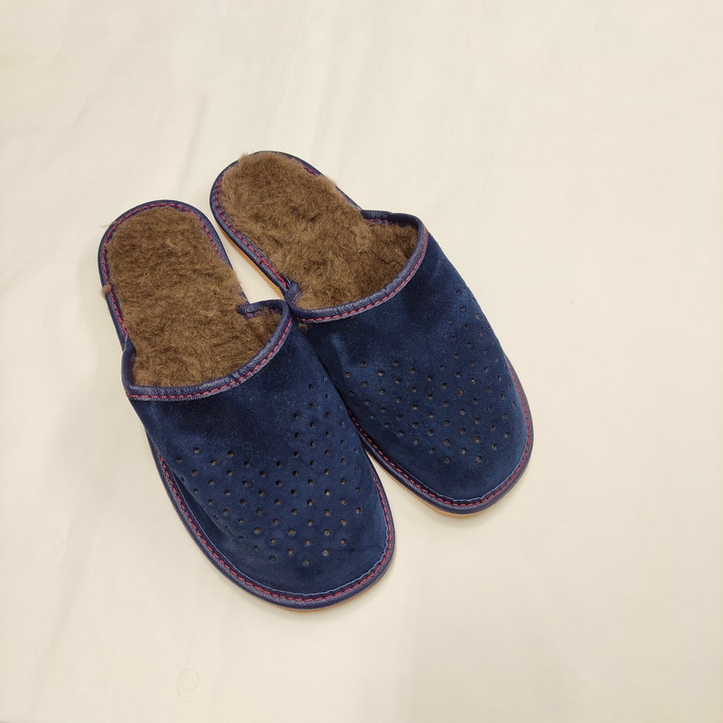 Puede incluir: Un par de zapatillas de ante azul marino con un dise&ntilde;o perforado en la parte superior. Las zapatillas tienen un interior marr&oacute;n y difuso y est&aacute;n ribeteadas con costuras rosas. Estas c&oacute;modas zapatillas est&aacute;n dise&ntilde;adas para uso en interiores.