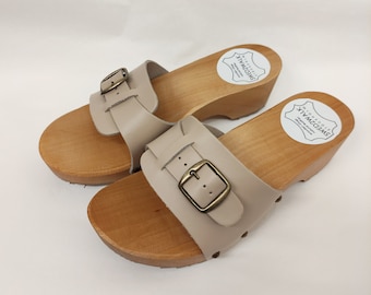 May include: A pair of beige leather sandals with wooden soles and buckles. The sandals have a label that says "Swedish clogs" on the sole.