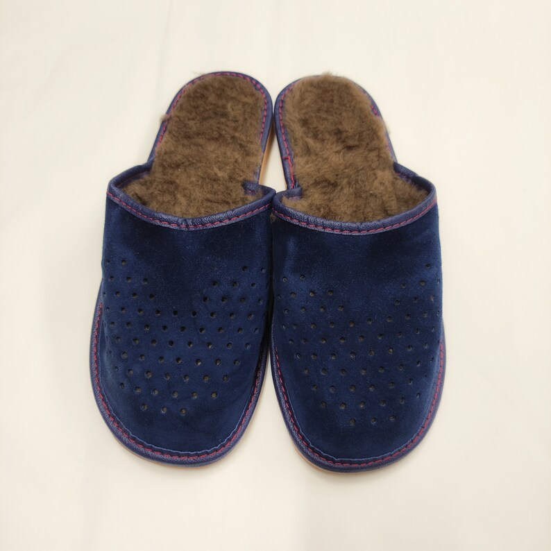 Puede incluir: Un par de zapatillas de ante azul marino con un dise&ntilde;o perforado. El interior est&aacute; forrado con piel marr&oacute;n y los bordes est&aacute;n ribeteados con costuras rojas. Estas zapatillas est&aacute;n dise&ntilde;adas para uso en interiores.