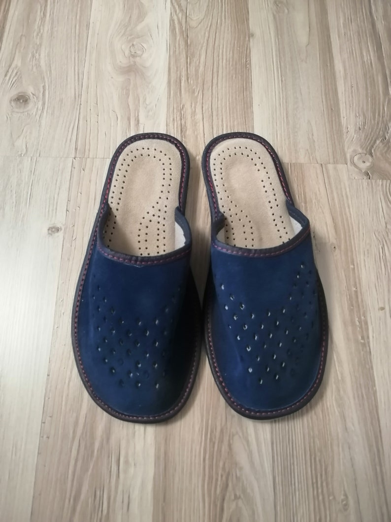 Puede incluir: Un par de zapatillas de ante azul marino. Las zapatillas tienen un dise&ntilde;o perforado en la parte superior, un interior beige claro con peque&ntilde;os orificios de ventilaci&oacute;n y un ribete rojo oscuro. Para uso en interiores.
