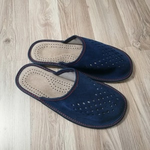 Puede incluir: Un par de zapatillas de ante azul marino con un dise&ntilde;o perforado en la parte superior. Las zapatillas tienen un interior marr&oacute;n claro y est&aacute;n ribeteadas con costuras rojas. Las suelas son de color azul oscuro.