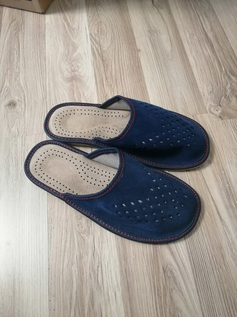 Puede incluir: Un par de zapatillas de ante azul marino con un dise&ntilde;o perforado en la parte superior. Las zapatillas tienen un interior marr&oacute;n claro y est&aacute;n ribeteadas con costuras rojas. Las suelas son de color azul oscuro.