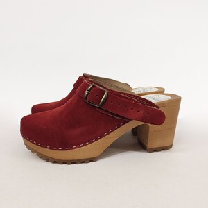 May include: Red suede heeled clogs with a buckle strap and a wooden platform sole.