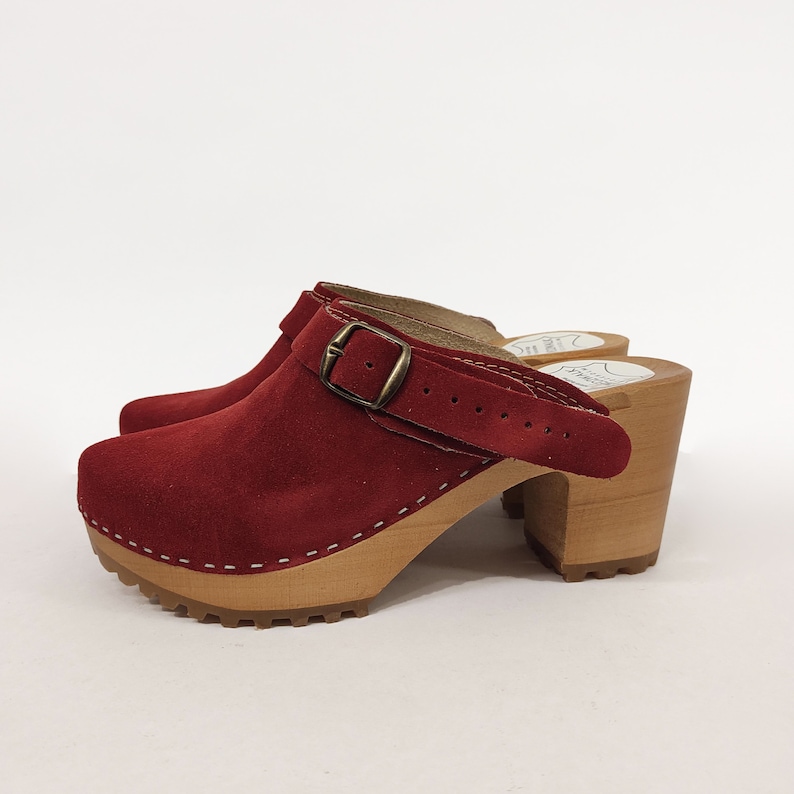 May include: Red suede heeled clogs with a buckle strap and a wooden platform sole.