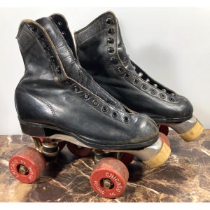 May include: A pair of vintage black roller skates with red and yellow wheels. The skates have black leather boots with eyelets for laces. The wheels are red with the text "CHICAGO" printed on them.