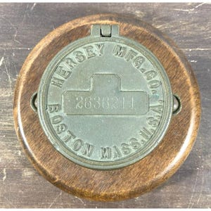 May include: A round wooden base with a metal cover. The cover has the text "HERSEY MFG. CO. BOSTON MASS." and the number "2636211" on it.