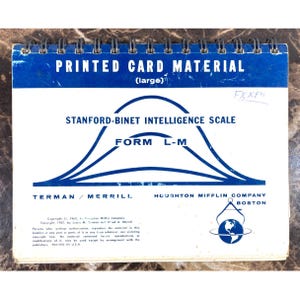 May include: A spiral-bound booklet with a blue and white cover. The cover reads "PRINTED CARD MATERIAL" and "STANFORD-BINET INTELLIGENCE SCALE FORM L-M." The booklet is from Terman/Merrill and Houghton Mifflin Company, Boston.