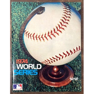May include: A vintage 1974 World Series program cover featuring a baseball on a wooden stand against a green grass background. The program cover has a price tag of $2.00.